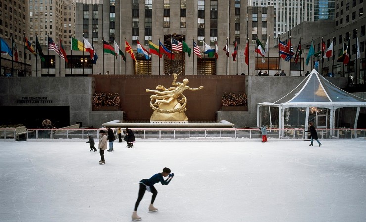 Ice skaters at Rockefeller Center in front of golden statue and national flags